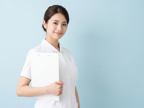 白いクリップボードを抱えてカメラを見つめるナース服の女性
