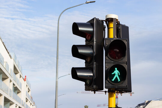 Green pedestrian traffic light illuminated on a street corner with modern buildings and a clear sky in the background, signaling safe crossing for pedestrians