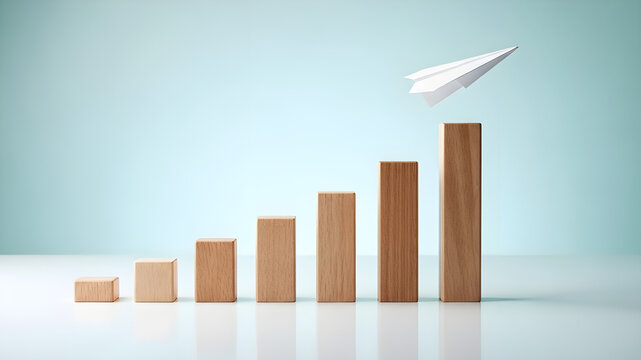 Paper airplane flying above wooden block bar chart showing business growth and financial success concept
