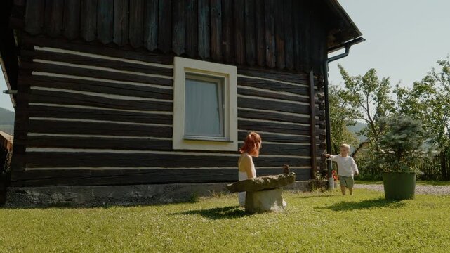 A woman and her little boy have fun in front of a traditional house in Bucovina. They enjoy their day in the sun and explore the area around the house.