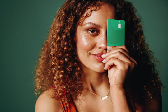 Confident woman showcasing green banking card in studio portrait