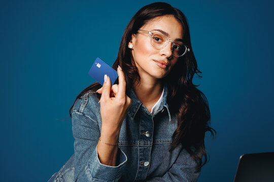 The woman uses a laptop while holding a credit card for online banking