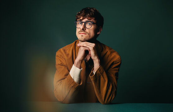 Thoughtful businessman with glasses at table in studio, reflecting on professional ideas