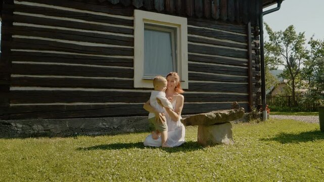 A woman sits outside a traditional house in Bucovina as her little boy runs to her and hugs her. They enjoy their time together in the sun.