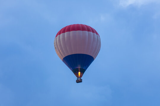 A low angle shot of a red, white, and blue hot air balloon flying high in the blue sky