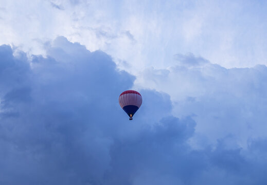 A hot air balloon flying among dramatic dark storm clouds in the blue sky