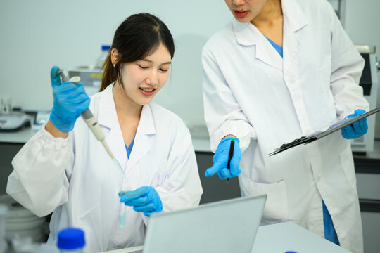 Asian Female Scientists Working Together in Laboratory with Pipette and Clipboard