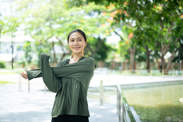 Fototapeta premium Young Asian Woman Stretching Arms in Green Park Before Workout Outdoors