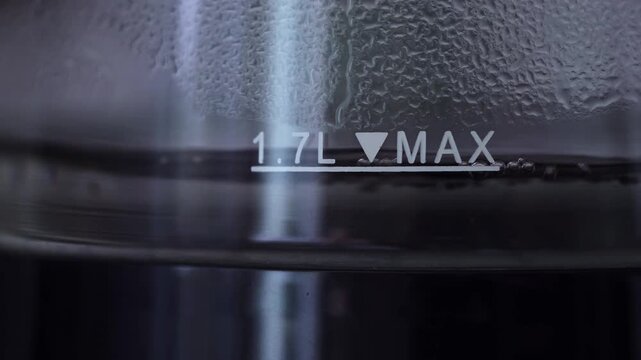 Macro shot water boiling vigorously in condensed glass kettle with 1.7L MAX marking visible.