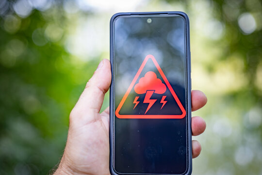 A warning about adverse weather conditions and thunderstorms is displayed on the smartphone screen outside.