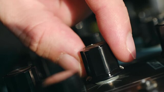 Close up sound engineer hand turning black plastic knob on professional mixing console, adjusting levels, parameters in recording studio, live music venue. Hand adjusting volume knob on mixing console