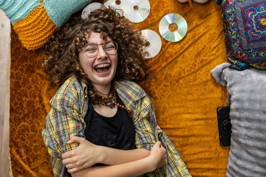 Laughing teenager lies on a bed with compact discs enjoying music