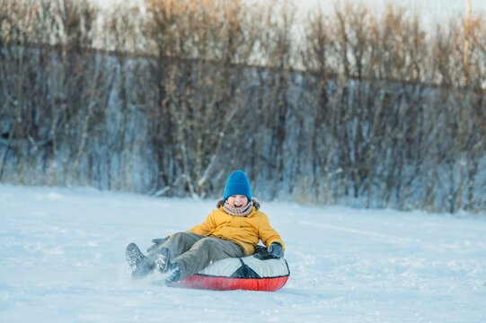 Child in yellow jacket sledding outdoors in winter with blue hat