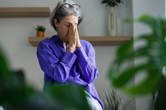 Woman with closed eyes and hands together experiencing stress indoors