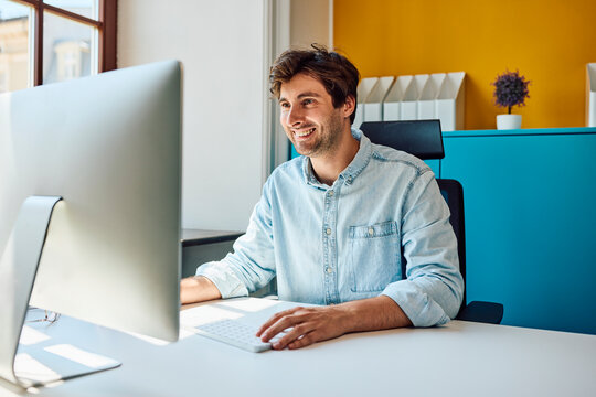 Smiling man uses a desktop computer at his colorful office desk