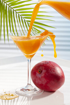Mango juice being poured in martini glass besides mango
