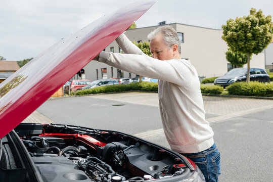 Driver opening the hood of a red car for engine inspection