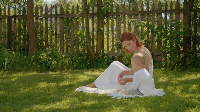 A woman sits on the grass with her little boy in the yard. They explore the plants around them and share moments of discovery while enjoying family time together.