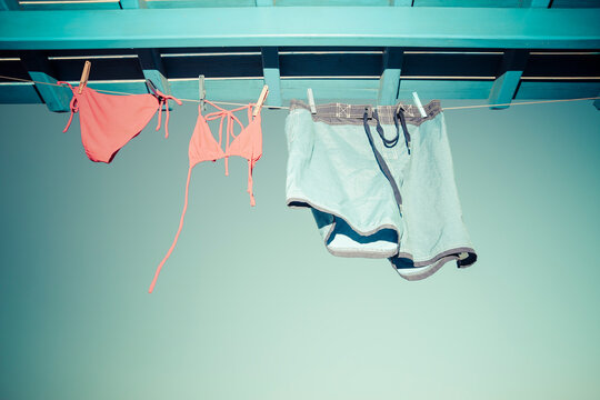 Bikini and bathing trunks hanging on clothes line under the roof