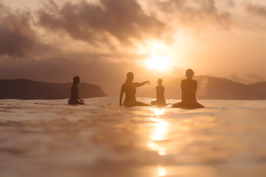 Indonesia, Lombok, group of surfers sitting on surfboards at sunset