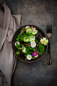 A fresh spring salad with edible flowers sits on a dark table