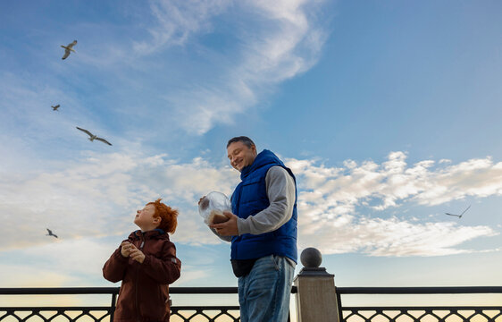 Father and son feed seagulls on a promenade by the beach