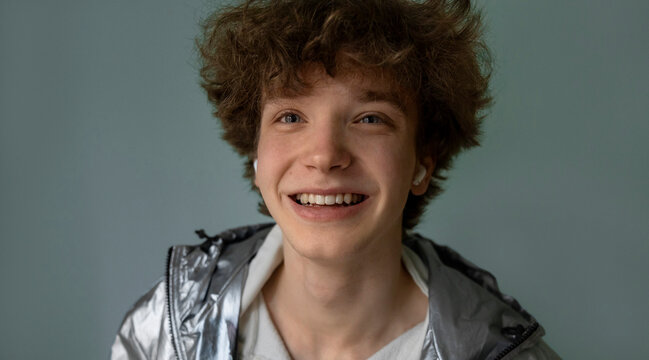 Smiling teenager in a shiny jacket listens to music indoors