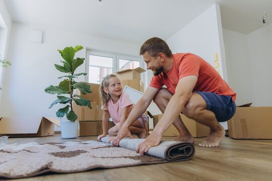 Father and daughter unpack and set up rug in new house living room