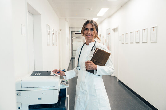 Doctor with stethoscope working with printer in hospital corridor