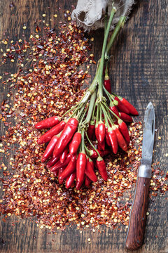 Bunch of red chili peppers, chili flakes and knife on wood