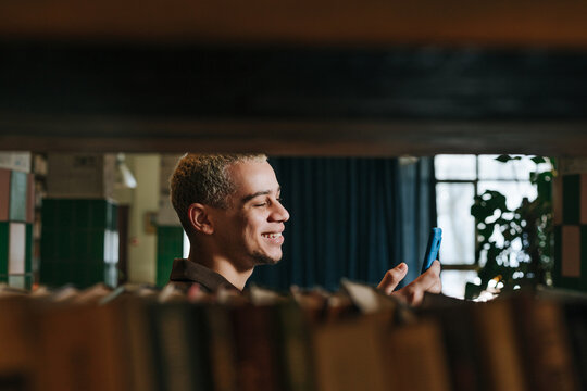 Smiling male student messaging on smartphone in library