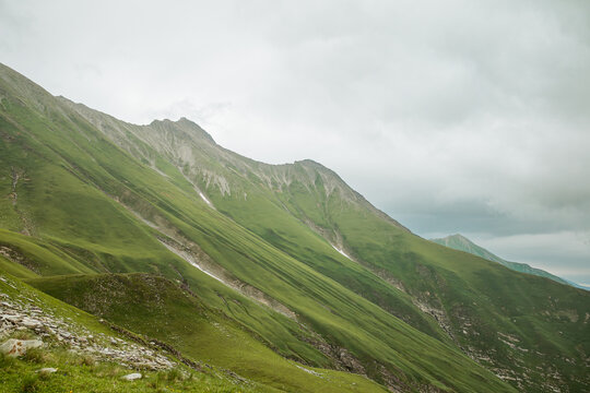 Epic green mountain peaks and deep valleys in the Greater Caucasus range, Georgia. Moody atmospheric landscape with low clouds and lush slopes.