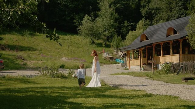 A woman and her little boy walk together in Bucovina near a traditional house. They share moments of joy while enjoying the green space around them.