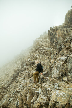 Male hiker climbing a steep, rocky mountain ridge in thick fog. Extreme hiking and mountaineering adventure in the Caucasus mountains, Georgia