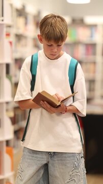Teenage boy stands in bookstore, browsing shelves and picking out book that interests him