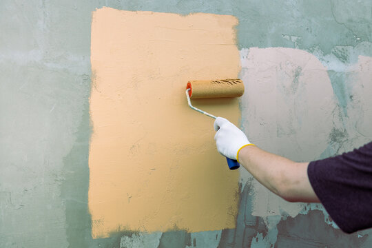 Hand rolls paint over rough wall surface