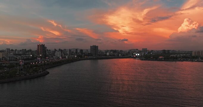 Beautiful sunset view of Mumbai, Maharashtra, with a dramatic orange sky illuminating the city skyline and calm waterfront. The glowing clouds, shimmering water, and striking evening cityscape.