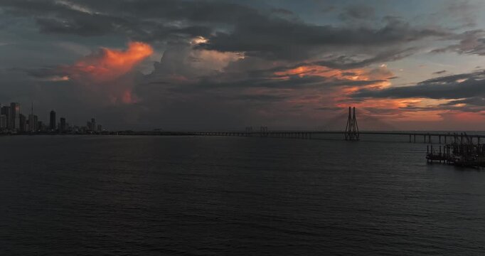 Beautiful sunset view of Mumbai, Maharashtra, with a dramatic orange sky illuminating the city skyline and calm waterfront. The glowing clouds, shimmering water, and striking evening cityscape.