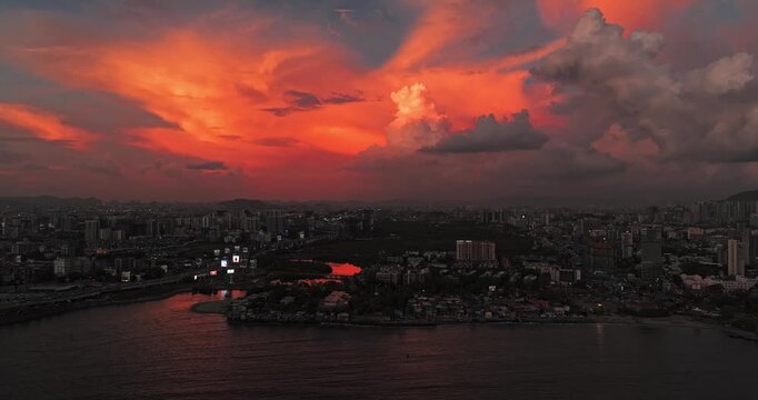 Beautiful sunset view of Mumbai, Maharashtra, with a dramatic orange sky illuminating the city skyline and calm waterfront. The glowing clouds, shimmering water, and striking evening cityscape.