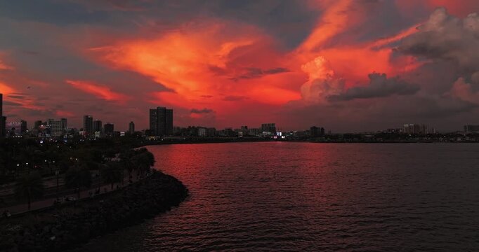 Beautiful sunset view of Mumbai, Maharashtra, with a dramatic orange sky illuminating the city skyline and calm waterfront. The glowing clouds, shimmering water, and striking evening cityscape.
