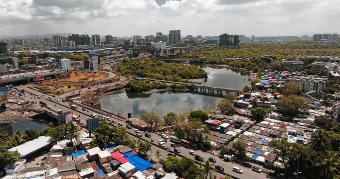 Aerial view of Mumbai, Maharashtra, India, showcasing busy roads, dense residential areas, green mangroves, a waterbody, and modern high-rise buildings.