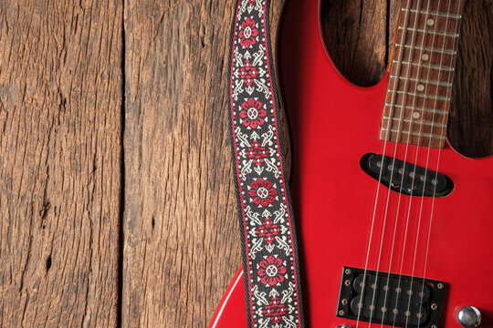 Top View of Red Electric Guitar with Vintage Strap on Rustic Wooden Background.