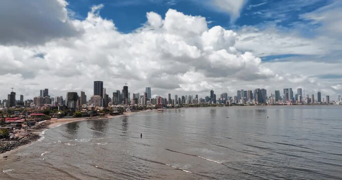 Beautiful aerial view of Mumbai city skyline along the Arabian Sea, featuring modern high-rise buildings, sandy beaches, and a vibrant coastal landscape under a bright blue sky.