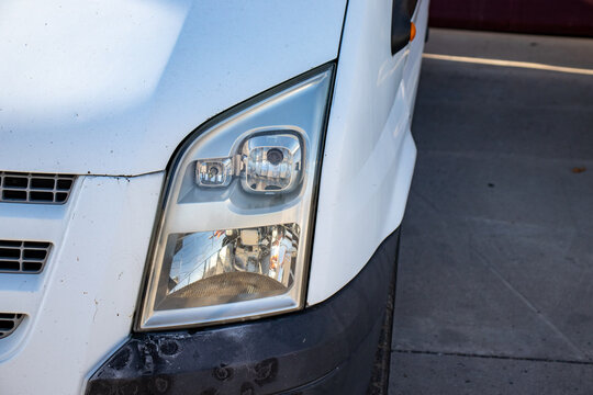 Close-up of a front headlight and bumper on a white commercial delivery van. Ideal for transportation, logistics, cargo delivery, auto parts, and commercial vehicle fleet concepts.