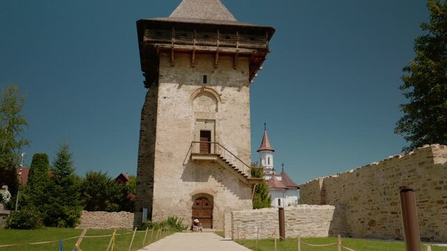 A mother and child stroll by the old walls and tower at Humor Monastery. They explore the area and admire the historic architecture during a sunny day.