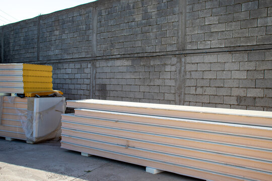 Stacked insulated sandwich panels stored outdoors near a concrete cinder block wall. Ideal for construction materials, building supply, thermal insulation, and industrial site concepts.