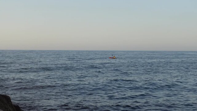 Man paddling kayak on ocean water waves in the distance cuts across the shot from right to left
