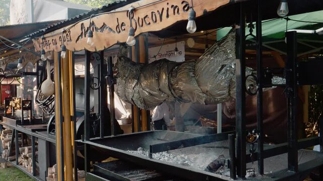 A street stall in Bukovina serves as a setting for a pig roasting on a protap. People gather to watch as the pig turns, cooking for the festival crowd.