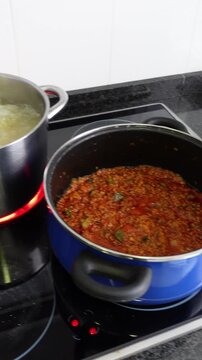 Vertical shot of two pots preparing pasta bolognese. One pot with the sauce and another with the pasta cooking. On a home electric stove
