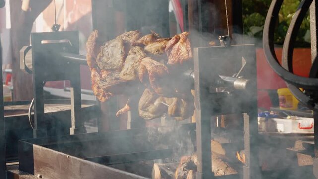 Chickens cook slowly on a rotating grill in Bukovina during a street food festival. Smoke rises as people enjoy the smell of grilled food.